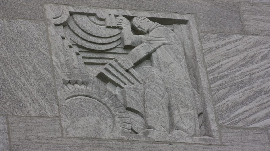 Carving on the upper area of the north and south extensions of City Hall, this is an Art Deco figure operating machinery, circa 2022.