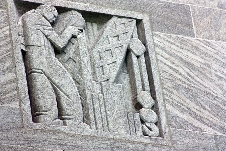 Carving on the upper area of the north and south extensions of City Hall, this is an Art Deco figure operating a crane type of machine, circa 2022.